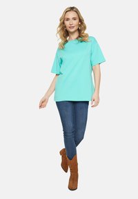 Turkos t-shirt med korta ärmar, avslappnad passform, ihop med mörkblå jeans och bruna ankelstövlar. Slät tyg utan mönster.