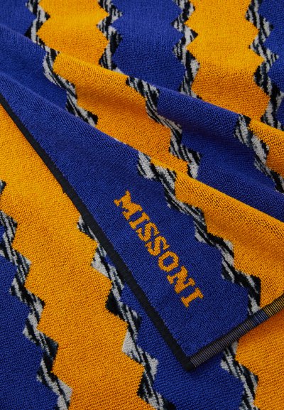 Pestrofarebný uterák s cik-cak vzorom v modrej, žltej a čiernej farbe. Mäkká, textúrovaná tkanina s vyšitou logom "MISSoni".