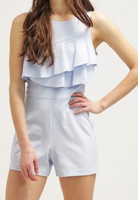 Světle modrý overal s vrstvou volánového výstřihu, přiléhavým korzetem a šortkami. Vyrobený z hladkého materiálu s čistým zakončením švů.