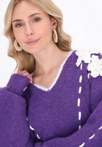 Pulover tricotat violet, pufos, cu decolteu în V, accente florale albe pe umăr și detalii de cusătură albă pe marginile mânecilor.