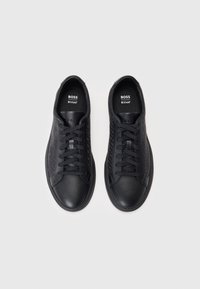 Baskets noires avec un bout en cuir lisse et des panneaux latéraux texturés. Elles présentent des lacets noirs et un logo sur la languette.