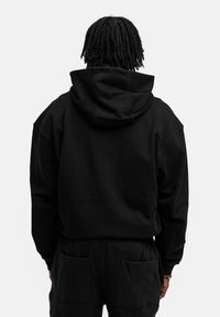Schwarzer, übergroßer Hoodie mit einer Kapuze und Zugband, nahtlosem Schulterdesign und weichem Material, kombiniert mit passenden schwarzen Hosen mit Taschen.
