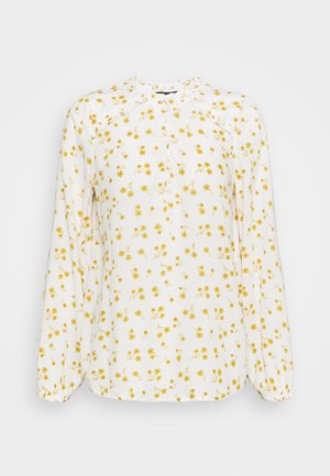 Witte blouse van lichtgewicht stof, met een geel bloemenpatroon, knoopsluiting aan de voorkant en lange mouwen met elastiek. Detail met ruches bij de halslijn.