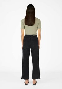 Zwarte wijdlopende jeans met een franjeszoom en twee achterzakken, gecombineerd met een fitted olijfgroen geribd T-shirt met korte mouwen.