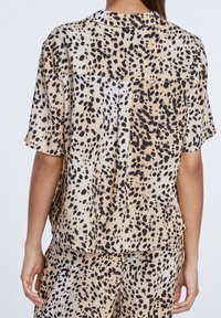Chemise à manches courtes beige avec imprimé léopard noir et marron. Dotée d'un col et d'une coupe décontractée avec un empiècement dos.
