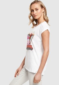 Valge puuvillane T-särk lühikeste volditud varrukatega, millel on graafiline print tegelasest ja sõna "Deadpool" julge punase tekstiga.