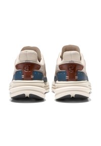 Ein Paar beige Sneakers mit braunen und blauen Akzenten, dicken, gerippten, weißen Sohlen, von hinten auf einem weißen Hintergrund gezeigt.