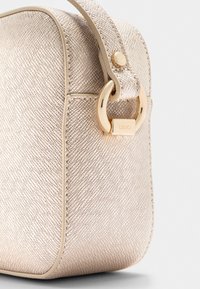 Borsa beige con texture caratterizzata da dettagli in metallo dorato e una forma arrotondata. La superficie presenta un motivo sottile e discreto.