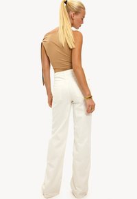Bodysuit asimétrico en tono beige combinado con pantalones de pierna ancha blancos de cintura alta. El atuendo presenta una textura suave y un diseño minimalista.