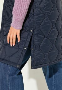 Námořnická prošívaná péřovka s patentkami na stranách, v kombinaci s světle růžovým žebrovaným svetrem, doplněná o modré džíny.