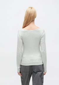 Γκρι ανοιχτόχρωμο μπλουζάκι με μακριά μανίκια και πλατύ ντεκολτέ, εφαρμοστή γραμμή και λείο ύφασμα, συνδυασμένο με γκρι παντελόνι με τσέπες cargo.