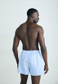 Himmelblaue karierte Boxershorts mit elastischem Bund, auf einem nackten Modell von hinten präsentiert, wodurch das Muster und die Passform hervorgehoben werden.