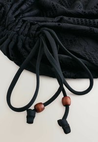 Tissu noir texturé avec deux cordons ajustables ornés de perles en bois marron sur un fond clair.