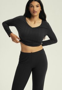 Black ribbed long-sleeve top with a v-neck, paired with matching high-waisted pants. The fabric has a smooth texture and a fitted design.