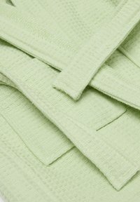 Lichtgroene, gestructureerde stofhanddoeken in lagen, met een wafelachtig patroon en gestikte randen voor duurzaamheid.