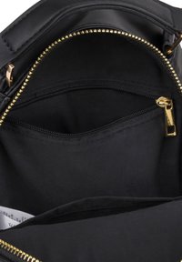 Intérieur de sac à main noir avec pochette zippée dorée et compartiment principal montrant la doublure en tissu et une étiquette blanche à l'intérieur.