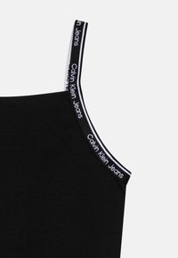 Czarny top bez rękawów z cienkimi ramiączkami i białym logo "Calvin Klein Jeans" na czarnym tle. Miękka, elastyczna tkanina.