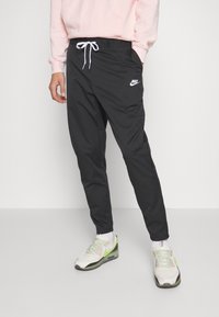 Černé sportovní kalhoty s bílým šňůrkem a logem Nike. Mají zúžený střih a měkký materiál, vhodné pro běžné nošení i aktivní pohyb.