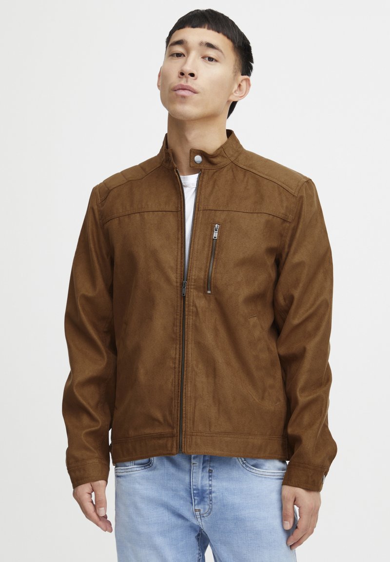 Veste en daim marron avec un col haut, fermeture éclair à l'avant et une poche poitrine. Présente une texture lisse et une silhouette ajustée.