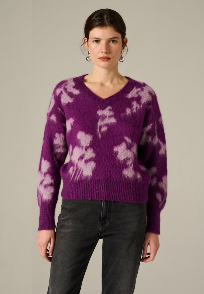 Pull en tricot violet à coupe ample, en col en V, avec un motif floral rose clair. Comprend des poignets et un ourlet côtelés, fabriqué à partir d'un matériau doux et texturé.