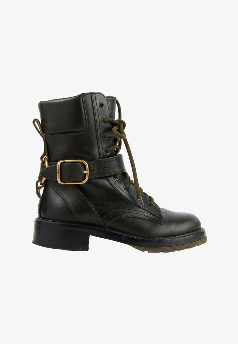 Bottine noire en cuir avec lacets, une bride latérale décorative avec boucle dorée et un petit talon carré sur fond blanc.