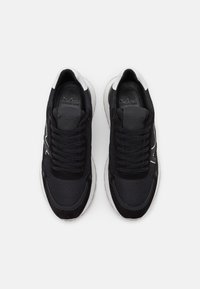 Černé tenisky s horní částí z síťoviny a semiše, kulatou špičkou, zavazováním na tkaničky a bílou gumovou podrážkou s logem.