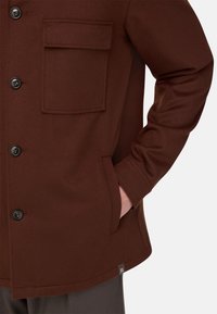 Braune Wollmischungjacke mit einer Brusttasche, Knopfverschlüssen und einer Seitentasche. Glatte Textur mit geradem Schnitt.