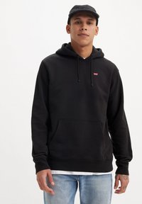 Zwarte hoodie met trekkoord en voorzak, met een klein rood logo. Gecombineerd met licht gewassen jeans. Glad oppervlak, casual pasvorm.