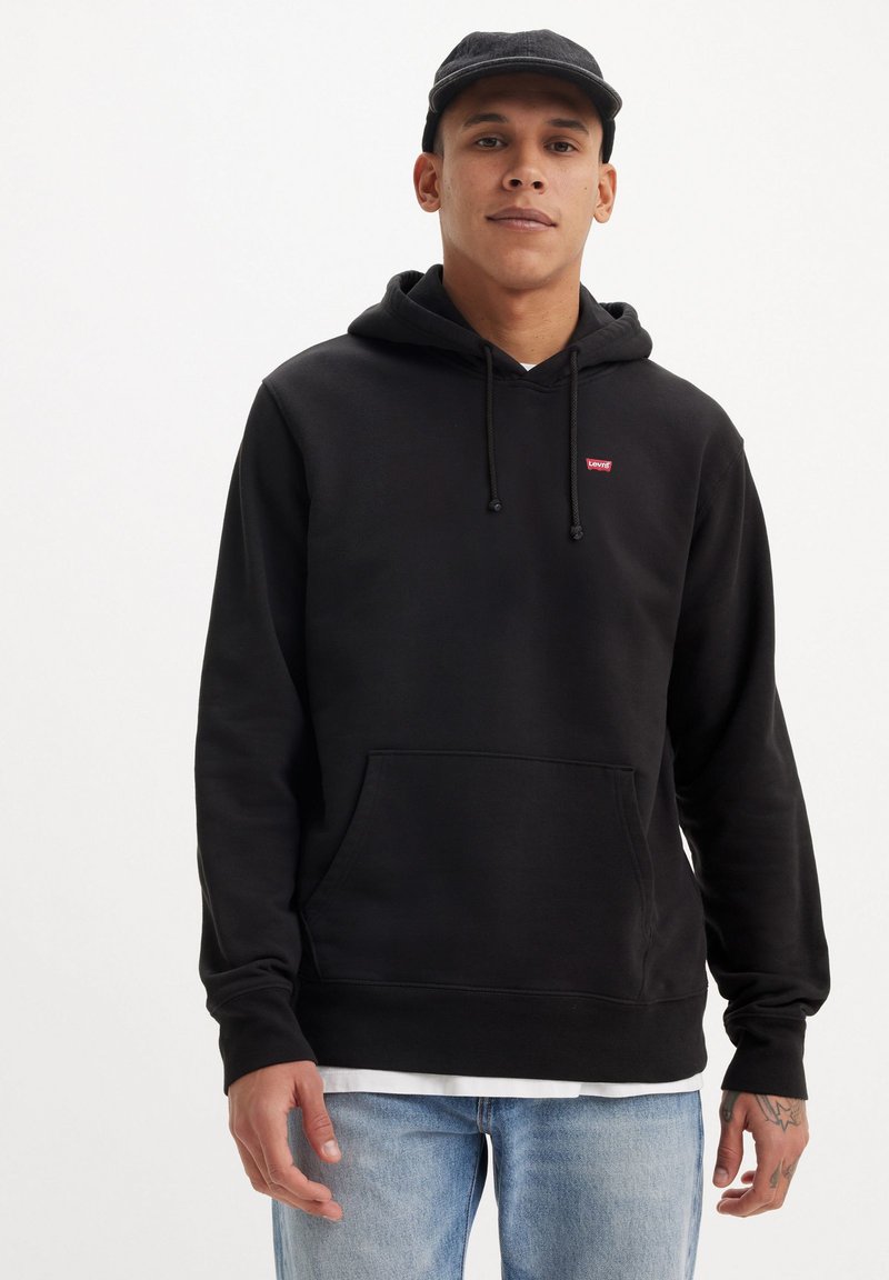 Zwarte hoodie met trekkoord en voorzak, met een klein rood logo. Gecombineerd met licht gewassen jeans. Glad oppervlak, casual pasvorm.