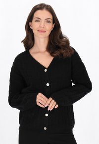 Zwarte gebreide cardigan met een textuurpatroon, V-halsontwerp en grote zilveren knopen aan de voorkant. Lange mouwen met ribgebreide manchetten.