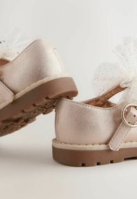 Rosa metallische Kinderschuhe mit runder Spitze, Klettverschluss und einer Tüllschleife mit Punkten. Sie verfügen über eine strukturierte Gummisohle.