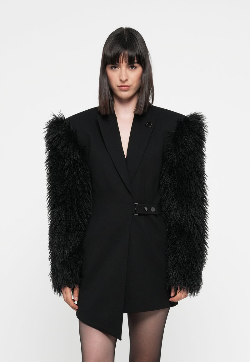 Black tailored blazer dress with voluminous black faux fur sleeves. Features a deep V-neck, single button closure, and asymmetrical hemline.