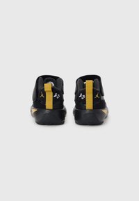 Czarne buty sportowe z żółtymi akcentami, z teksturowaną cholewką, wzmocnionym piętą i charakterystycznym logo z tyłu.