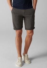Shorts gris enroulés en tissu en mélange de coton, dotés de poches latérales et d'une taille plate, assortis à des baskets de couleur claire.