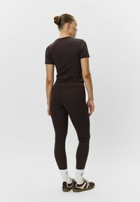 Brązowy dopasowany top z krótkim rękawem i legginsy wykonane z gładkiego materiału, połączone z białymi i brązowymi trampkami oraz białymi skarpetkami.