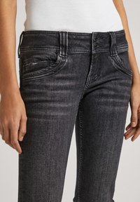 Czarne dżinsy o slim fit, z średnim stanem, dwoma przednimi kieszeniami i subtelnym wyblaknięciem. Zawierają podwójne zapięcie na guziki.