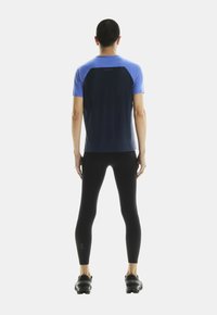 Koszulka sportowa w niebieskim i granatowym kolorze o dopasowanym fasonie, zestawiona z czarnymi legginsami i butami sportowymi, podkreślająca warstwowy kolor i teksturę.