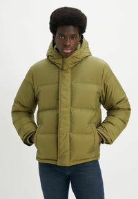 Chaqueta acolchada verde oliva con capucha, diseño acolchado y cierre frontal con cremallera. Incluye un pequeño parche con logo en el pecho.