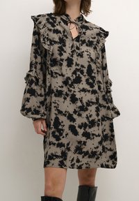 Vestido ligero con un patrón de tie-dye en negro y beige, que presenta mangas con volantes y un detalle de escote con forma de ojal.