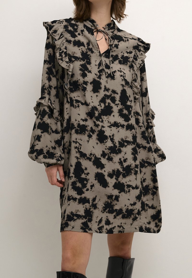 Vestido ligero con un patrón de tie-dye en negro y beige, que presenta mangas con volantes y un detalle de escote con forma de ojal.