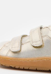 Dziecięce buty na rzepy z metaliczno-złotą syntetyczną cholewką, gumową podeszwą i subtelnymi detalami przeszycia. Wysoka cholewka z wyściółką przy kostce.