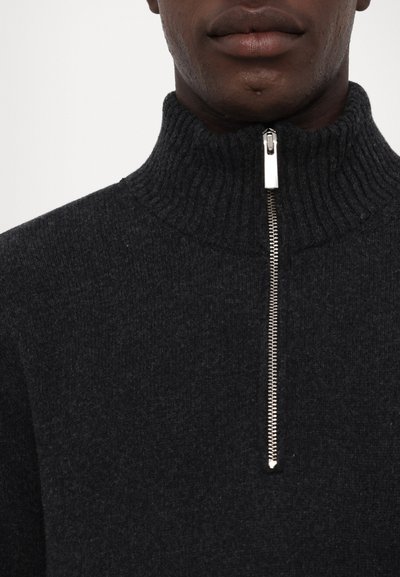 Mörkgrå zip-neck tröja i mjukt tyg, med en ribbad krage och detaljer med metalldragkedja vid halsen.