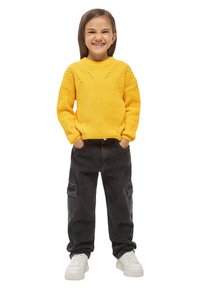 Maglione giallo lavorato a maglia con scollo rotondo e motivo testurizzato, abbinato a pantaloni cargo neri e sneakers bianche.