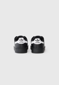 Čierne kožené tenisky s bielymi akcentmi, s vystuženým golierom, plochými šnúrkami a textúrovanou gumovou podrážkou. Logo Adidas zobrazené na päte.