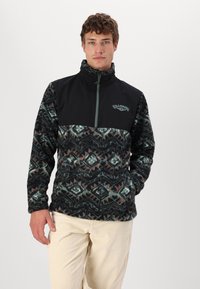 Fleece pullover met een zwart bovenstuk en een gewatteerd onderstuk met geometrische patronen in donker groen, teal, en rode accenten. Halve rits.