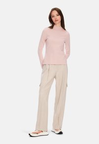 Helles rosa Langarmoberteil mit einem Stehkragen, kombiniert mit beigen weit geschnittenen Hosen mit Seitentaschen und texturiertem Stoff. Schwarz-weiße Sneaker.