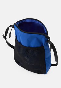 Sac bleu avec un extérieur en nylon et une poche avant en mesh noir. Il dispose d'une fermeture éclair et d'une sangle réglable. Doublure intérieure en bleu uni.