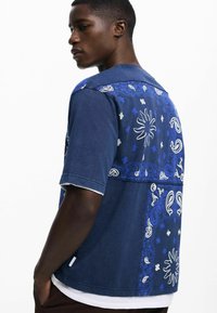 Kortærmet skjorte i mørkeblå denim med hvide paisley- og solmønstre. Har kontrasterende tekstur og et afslappet fit design.