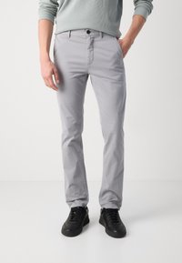 Light gray trousers with a slim fit, made from cotton, featuring a button closure and side pockets, paired with black sneakers.
