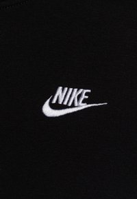 White embroidered Nike logo with swoosh on black fabric background, centered in the frame.